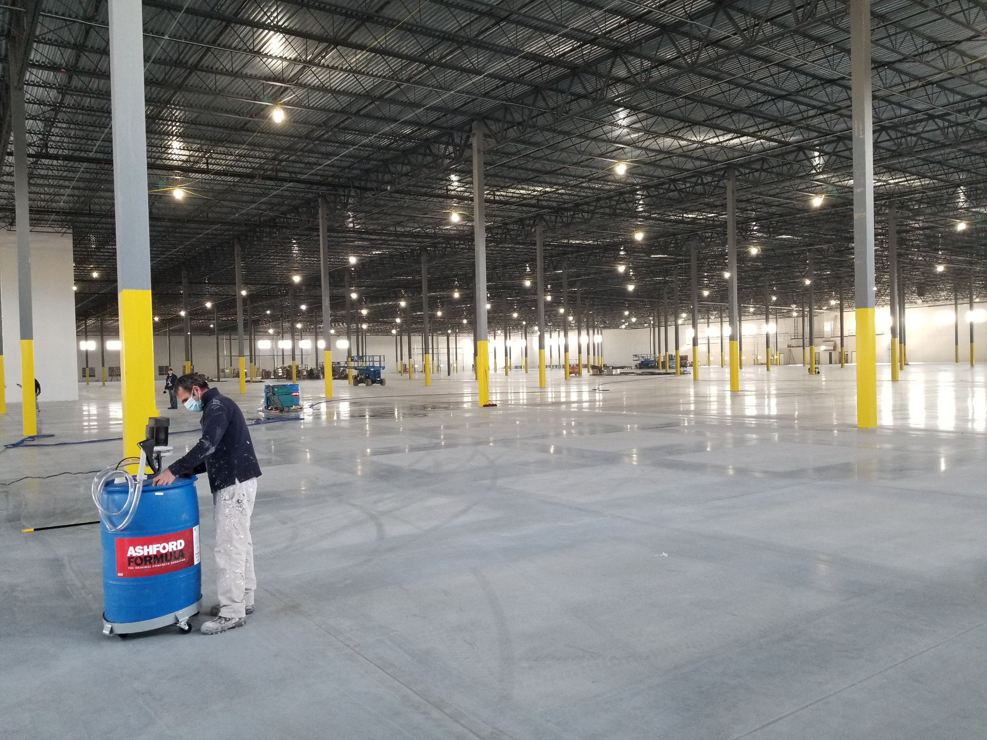 Never Boring Flooring applicator spraying Ashford Formula across a Highland Park warehouse slab