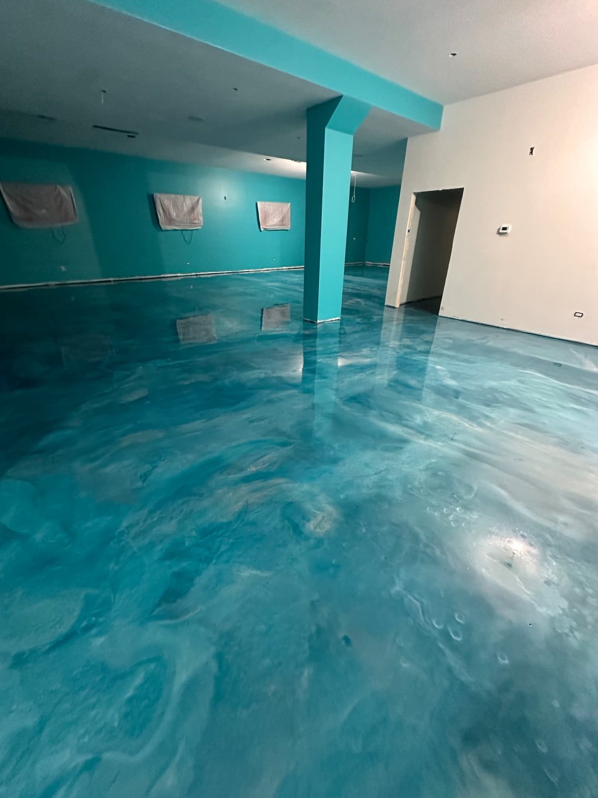 Turquoise Metallic Pour — A bold turquoise and pearl marble effect poured wall to wall in an open commercial space.